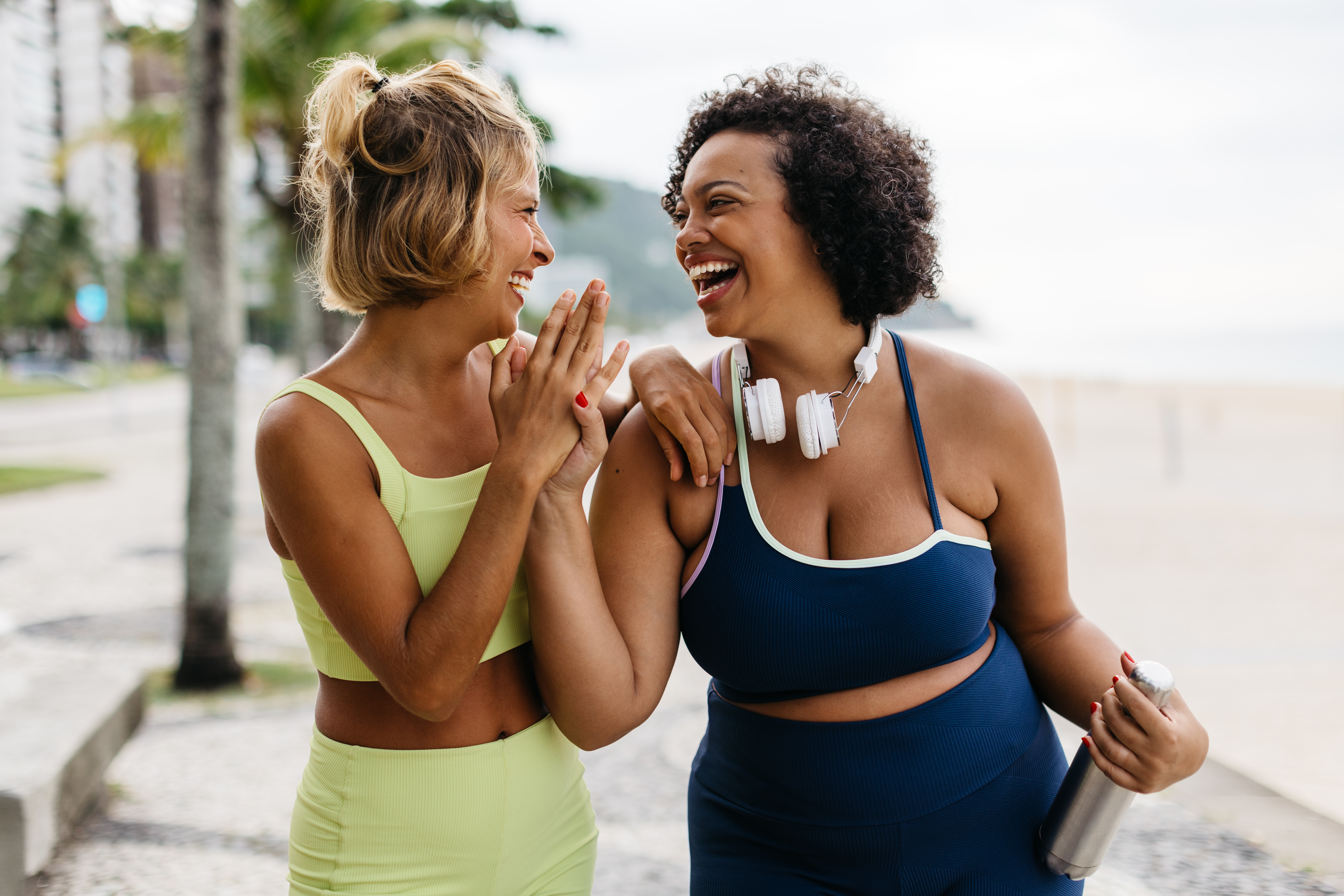 two women exercising at the beach, laughing and talking.